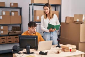 Emprendedores configurando una tienda online desde un ordenador portátil con productos y cajas de envío